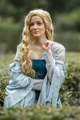 Obraz premium A young beautiful girl in a summer park. A beautiful medieval elf princess in a blue dress in the forest