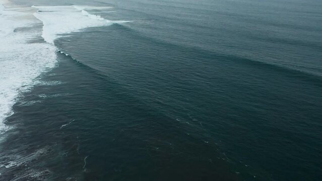Peaceful majestic aerial footage of dark turquoise ocean waves rolling on shore and crashing with white foam. Copter top footage of set of giant sea waves. Drone slow motion view of powerful sea swell