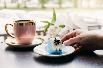 Blue macaroon dessert, original and stylish dessert in cafe in front of window, Hand holding plate with tasty sweet 