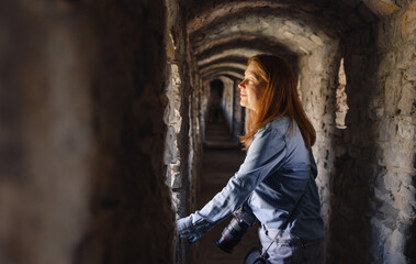 Woman walking through old tunnel, looking in window and taking pictures. Female visiting castle. Traveling in ancient building 