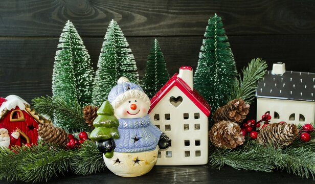 New Year's card, porcelain toy snowman with a Christmas tree in his hands and a New Year's forest house, green Christmas trees and a wooden sleigh.  Home decoration.  Background picture.