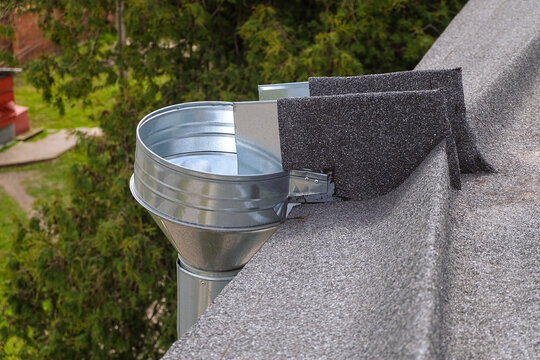 Metal galvanized water inlet funnel on the edge of a soft flat roll roof. External organized drainage system.