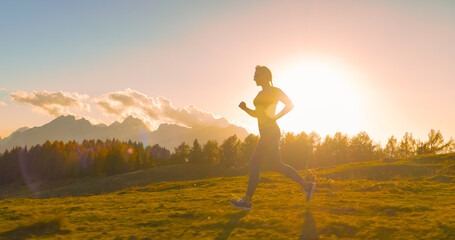CLOSE UP, LENS FLARE: Female runner jogging in sunset light along a scenic trail