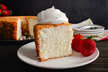 Slice of Angel Food Cake Topped with Whipped Cream and Strawberries: Piece of sponge cake on a plate with whipped topping and strawberry garnish