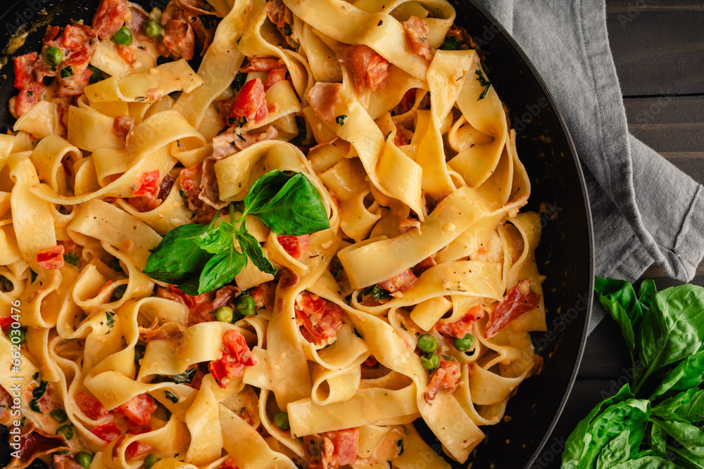 Wall mural pappardelle pasta in tomato cream sauce with peas and prosciutto: italian-style wide noodles in a sk