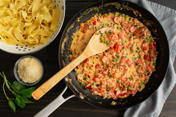 Tomato Cream Sauce with Peas and Prosciutto in a Large Skillet: Freshly made pasta sauce with a colander of broad pappardelle noodles on the side - obrazy, fototapety, plakaty