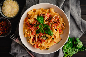 Pappardelle Pasta in Tomato Cream Sauce with Peas and Prosciutto: Italian-style wide noodles in a pasta bowl with basil and grated parmesan cheese