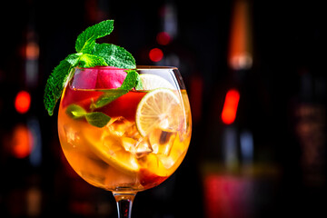 Pink sangria alcoholic cocktail drink with rose wine, peach, orange, lime and ice. Black bar counter background, steel bar tools and bottles