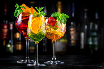 Red, white, pink sangria cocktail drinks with spanish wine, fruits, citrus and ice. Black bar counter background, steel bar tools and bottles