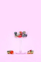 Cocktail glass and Christmas decorations on pastel pink background. Minimal Creative Christmas concept. Gold, green and red Christmas baubles in a cocktail glass and around. Happy New Year shot.