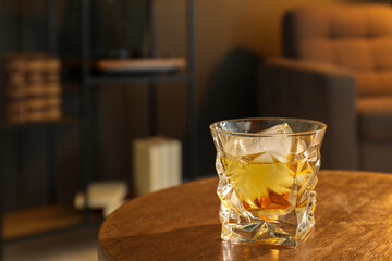 Glass of whiskey on wooden table in room, space for text. Relax at home