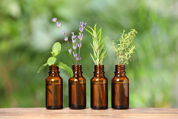 Bottles with essential oils and plants on wooden table against blurred green background