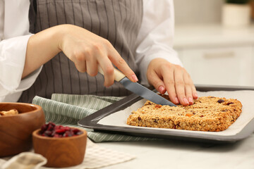 Woman cutting granola bars at table in kitchen, closeup