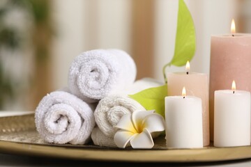 Fototapeta na wymiar Spa composition. Burning candles, plumeria flower, green leaves and towels on tray, closeup