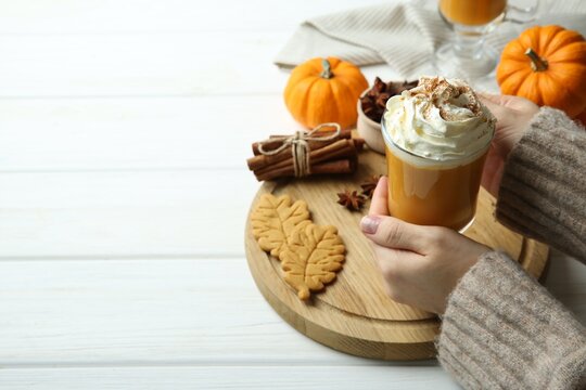 Woman holding cup of tasty pumpkin spice latte with whipped cream at white wooden table, closeup. Space for text