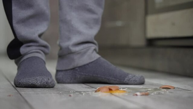 A guy in the kitchen dropped a chicken egg on the floor and it broke close-up