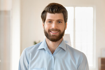 Happy young bearded entrepreneur man posing in office with white board in background, looking at...
