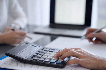 Two accountants use a calculator and laptop computer for counting taxes or revenue balance. Business, audit, and taxes concepts