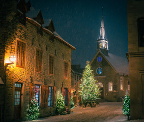 Fototapeta premium Christmas card: Magical Place Royale, Notre-Dame-des-Victoire Church, illuminated Christmas decorations and trees on a snowy night, Petit-Champlain District, Old Quebec City, Canada (December 2022).