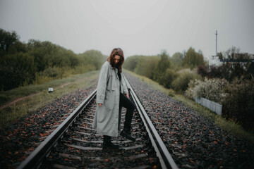 beautiful woman in a gray coat on the railway in gloomy and depressive weather. The concept of...