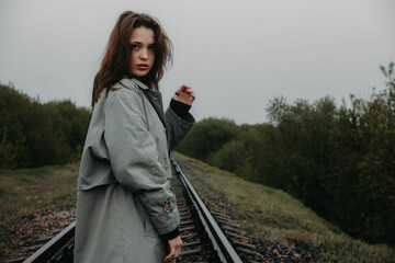 beautiful woman in a gray coat on the railway in gloomy and depressive weather. The concept of...