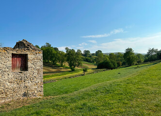 Obraz premium View past a derelict stone barn, with fields, old trees, and hills, on a late summers day near, Aysgarth, UK