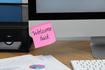 Sticky note with phrase Welcome Back on computer monitor in office
