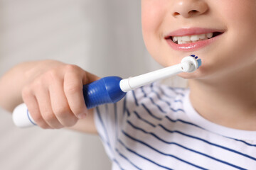 Little girl brushing her teeth with electric toothbrush on blurred background, closeup