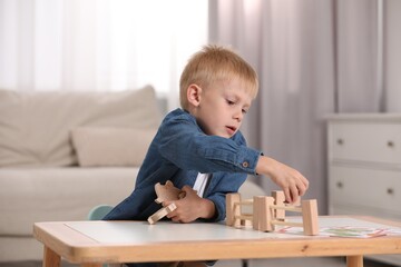 Fototapeta na wymiar Cute little boy playing with set of wooden animals and fence at table indoors. Child's toy