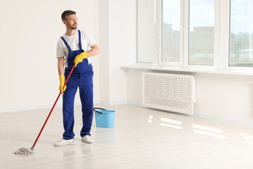 Man in uniform cleaning floor with mop indoors. Space for text - obrazy, fototapety, plakaty