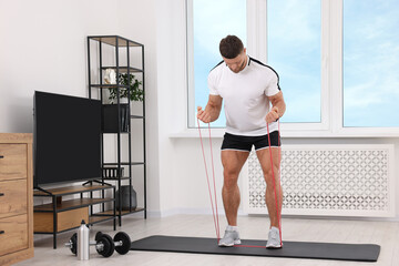 Fototapeta na wymiar Athletic man doing exercise with elastic resistance band on mat at home