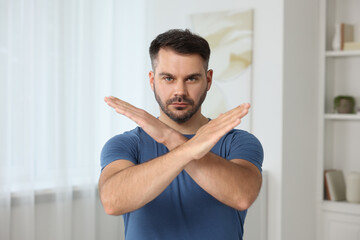 Handsome man with crossed hands at home. Stop gesture