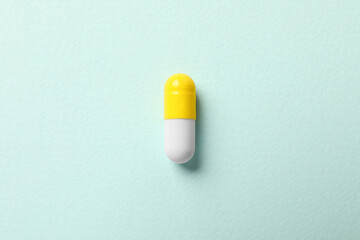 Fototapeta na wymiar One colorful pill on mint background, top view
