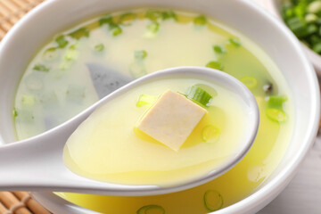 Eating delicious miso soup with tofu from bowl on table, closeup