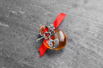 Heart shaped bottle of love potion with small key and padlock on grey table
