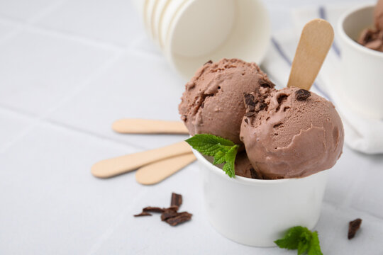 Paper cups with tasty chocolate ice cream on white tiled table, closeup. Space for text