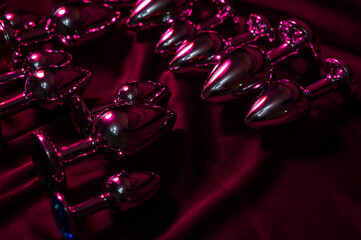 Lots of metal butt plugs in neon pink light. 