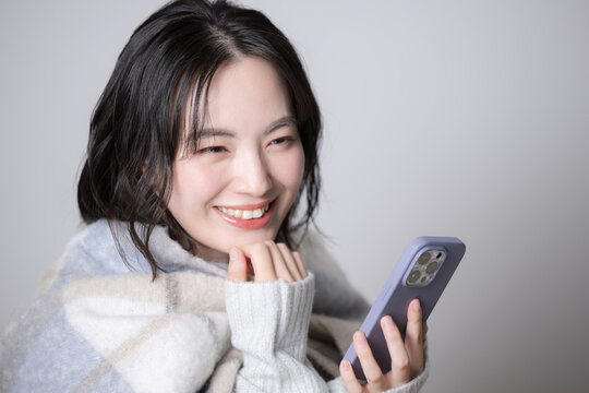 Fall and winter image of a young smiling woman operating a cell phone.