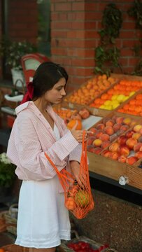 In a European store, a lively young lady with a pink hair bow is selecting fruits.