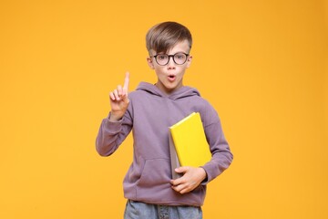 Surprised schoolboy in glasses holding books on orange background