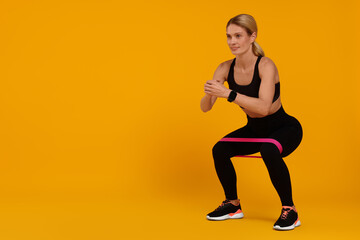 Woman exercising with elastic resistance band on orange background. Space for text