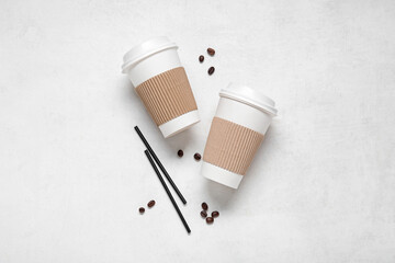 Takeaway paper cups with coffee beans and straws on white background