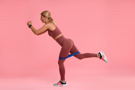 Woman exercising with elastic resistance band on pink background © New Africa