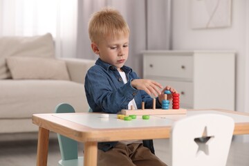 Cute little boy playing with stacking and counting game at table indoors. Child's toy