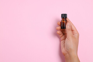 Woman with bottle of essential oil on pink background, closeup. Space for text