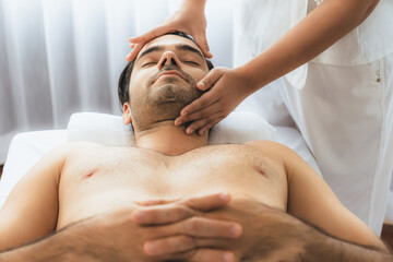 Caucasian man enjoying relaxing anti-stress head massage and pampering facial beauty skin recreation leisure in dayspa modern light ambient at luxury resort or hotel spa salon. Quiescent