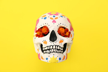 Painted human skull for Mexico's Day of the Dead (El Dia de Muertos) with flowers on yellow...