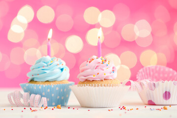 Tasty Birthday cupcakes with burning candles on table against blurred lights