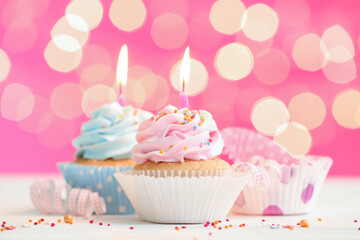 Tasty Birthday cupcakes with burning candles on table against blurred lights