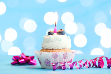 Tasty Birthday cupcake with burning candle and blueberries on table against blurred lights